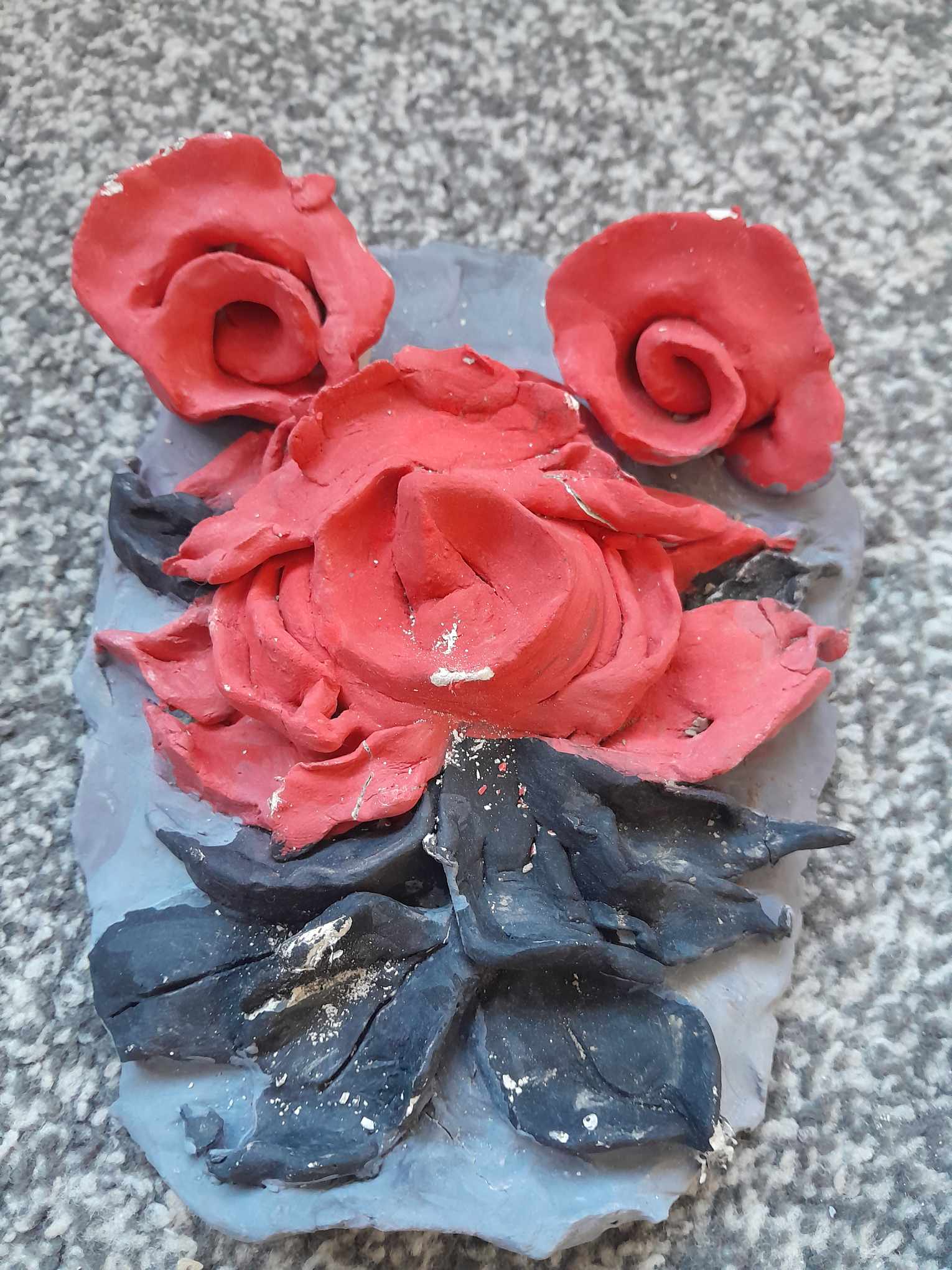 Sara went to the Prince's Trust and did a week of photography along with learning to use clay and she created a Rose theme clay piece that is just clayed as one rose with leaves embedded into the piece. She decided to paint the clay to show the details of the clay that was formed by using black on the leaves red on the rose and grey for the background to finish.